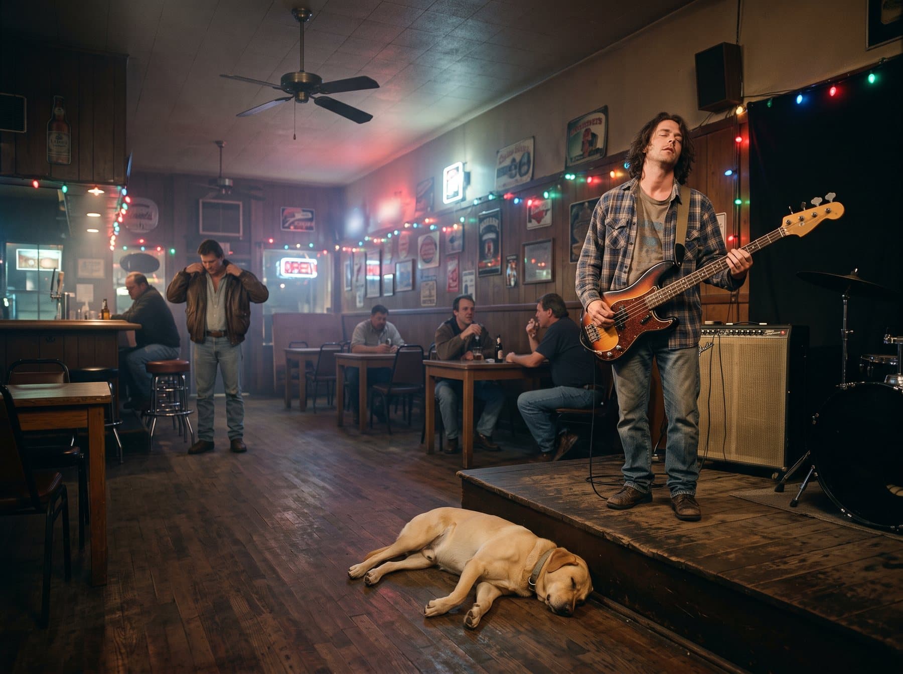 A lone bass player on a small stage in a nearly empty bar, a dog asleep on the floor in front of him